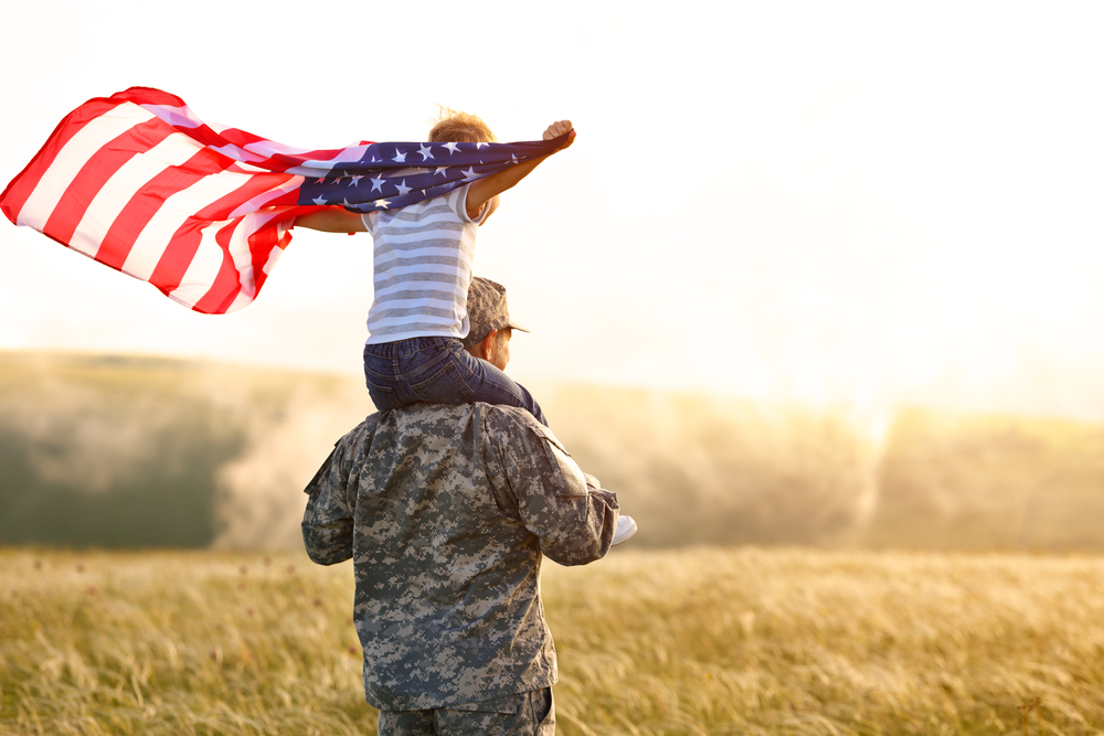 Rear view of military man father carrying happy little son with american flag